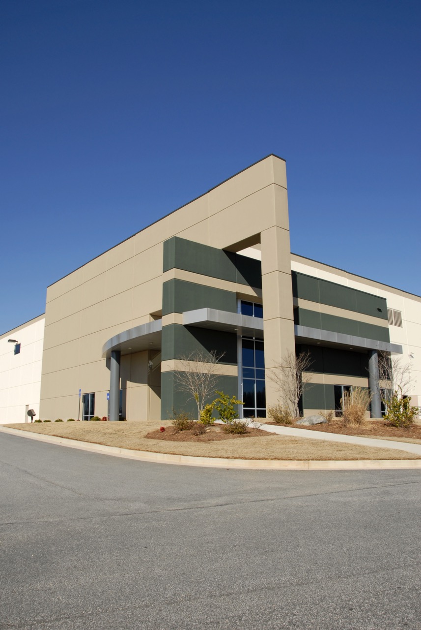 A modern industrial or office building with geometric architecture, featuring beige and dark green exterior walls, large windows, and a rounded entrance—ideal for businesses seeking quality property management cleaning services.